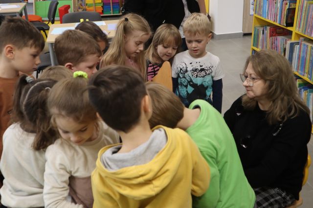 dzieci stoją, a przed nimi siedzi kobieta w czarnej bluzce