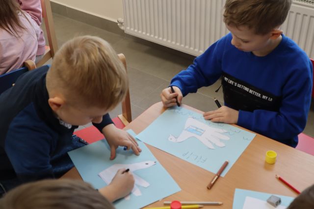 dzieci siedzące przy brązowych stołach rysują na kartkach łabędzie