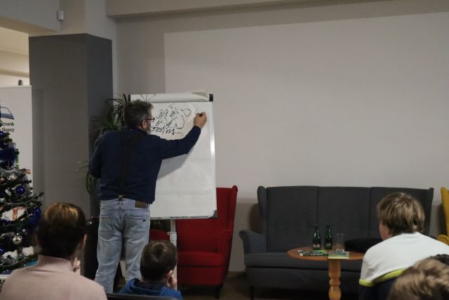 mężczyzna w ciemnym swetrze i jasnych dżinsach rysuje na dużej kartce