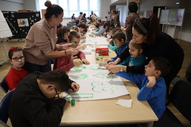 młodzież siedzi przy długim rzędzie stołów i maluje