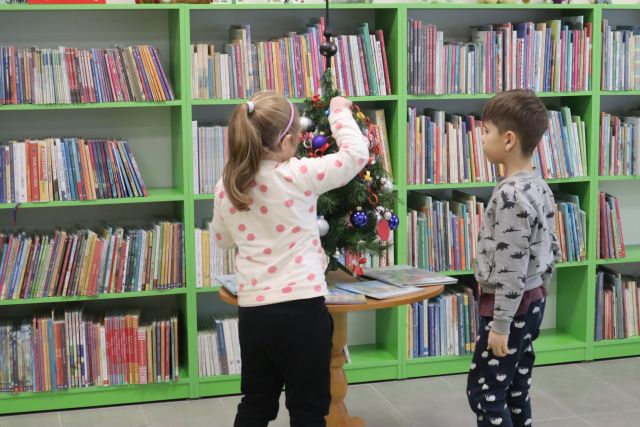 dziewczynka i chłopiec ubierają małą choinkę w wykonany przez siebie łańcuch, w tle regały z książkami