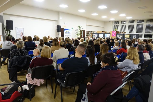 uczestniczy spotkania (około 150 osób) siedzą na krzesłach, w tle pomieszczenia biblioteczne