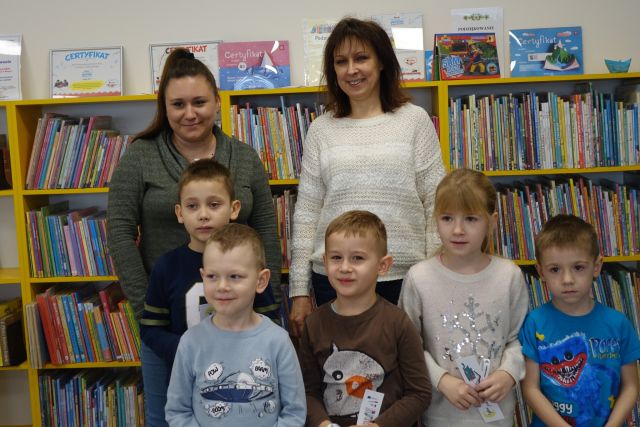 5 dzieci i dwie kobiety pozują do zdjęcia, w tle regały z książkami