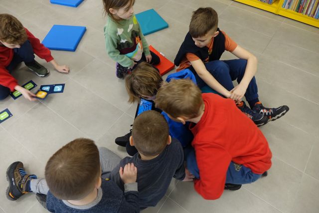 dzieci siedzą na podłodze i sterują robotami za pomocą tabletów