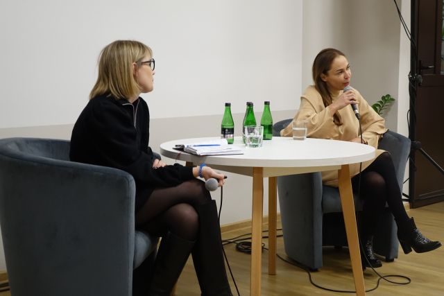 kobieta w czarnej sukience i kobieta w kremowej sukience siedzą przy biały okrągłym stoliku