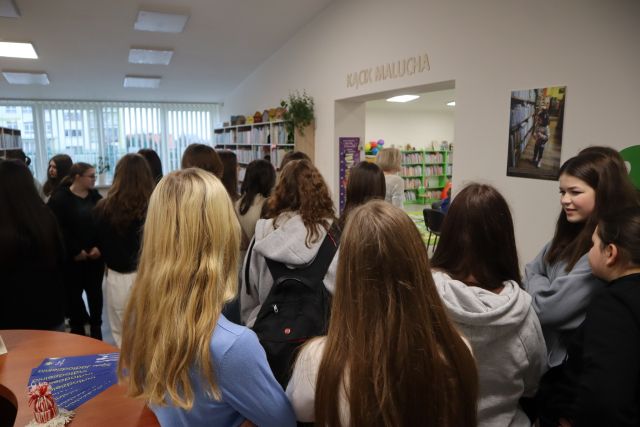 młodzież zwiedza część biblioteczną dla najmłodszych z kolorowymi regałami i zielonym dywanem