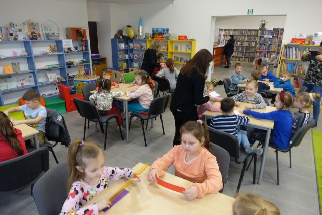dzieci siedzą przy stolikach i wykonują zakładki do książki, w tle regały kolorowe