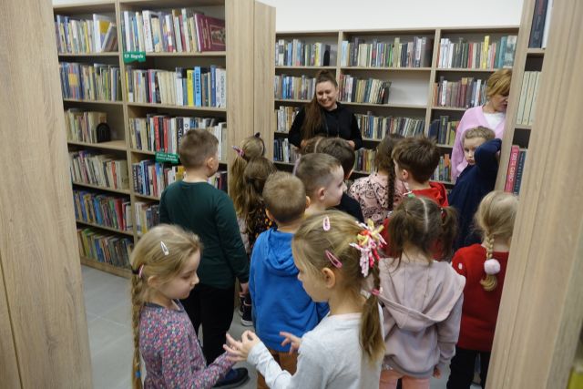 dzieci zwiedzają pomieszczenia biblioteczne, spacerują pomiędzy regałami z książkami
