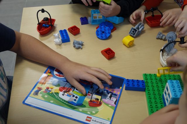 na stoliku dłonie dzieci układają z klocków lego