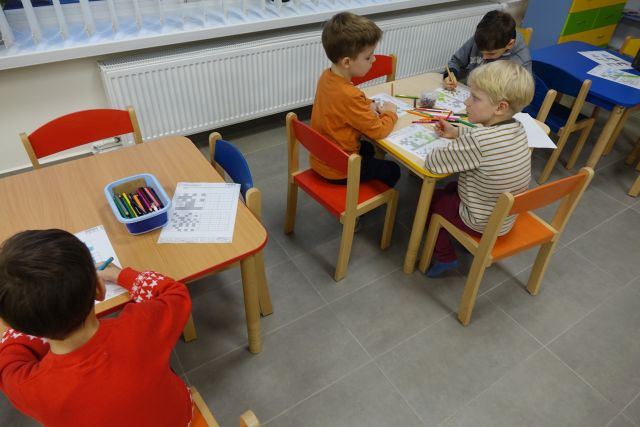 dzieci siedzące przy stolikach rozwiązują krzyżówki