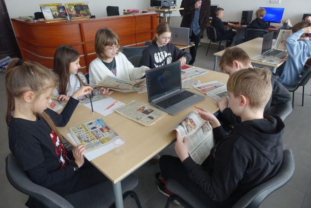 młodzie uczestnicy warsztatów siedzą przy laptopach, na stołąch leżą gazety