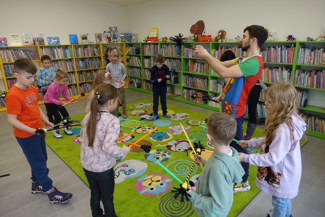 dzieci robią sztuczki cyrkowe z kijkami, w tle regały z książkami