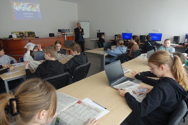 młodzi uczestnicy warsztatów siedzą przed laptopami i komputerami , przeglądają gazety