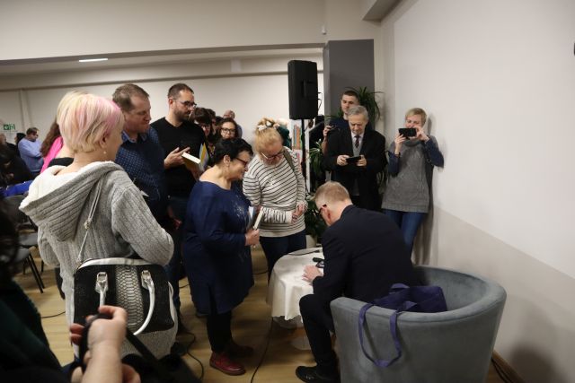 mężczyzna podpisujący książki, przed nimi stoją uczestnicy spotkania czekający na autograf