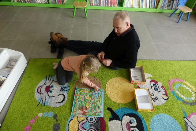 dziewczynka i osoba dorosłą siedzą na zielonym dywanie i grają w gry planszowe