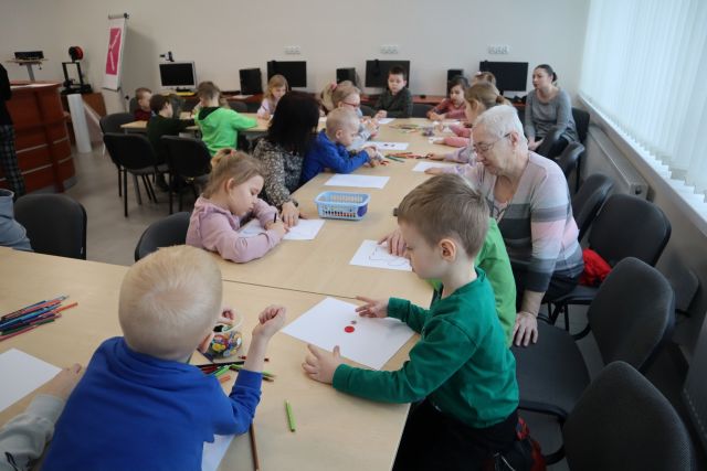dzieci siedzą przy stołach i wyklejają guzikami misie