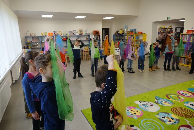 dzieci stoją i wykonują ćwiczenia z chustami, w tle regały z książkami