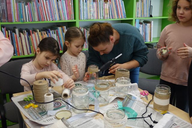 kobieta klei pistoletem z klejem sznurek do słoika, wokół niej 3 dziewczynki