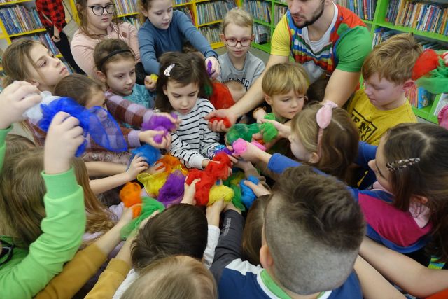 dzieci zgromadzone w grupie trzymają wyciągnięte ręce do środka i trzymają kolorowe chusty