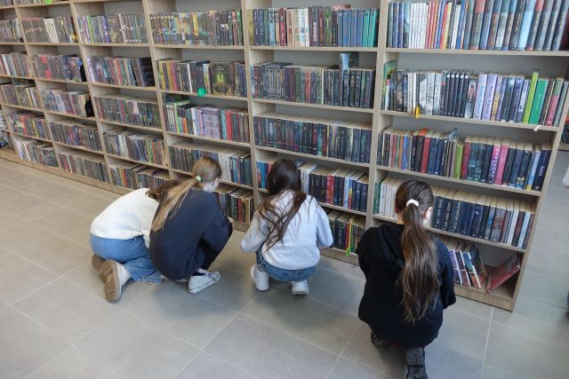 4 dziewczyny szukają ukrytego przedmiotu wśród książek na regałach