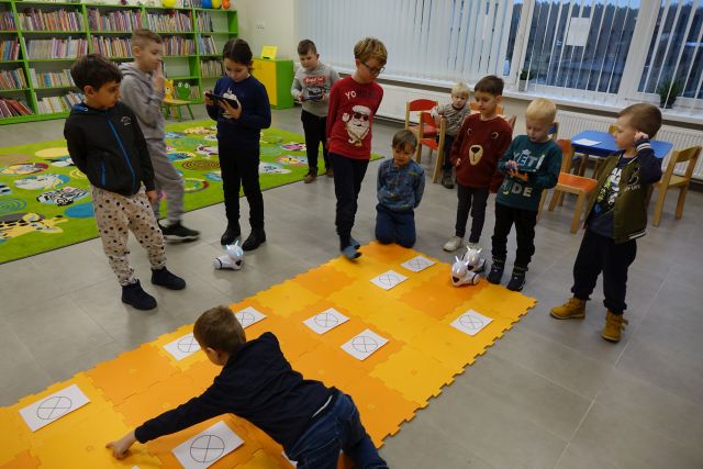 dzieci sterują robotami przy pomocy tabletów, roboty jeżdżą po pomarańczowej macie