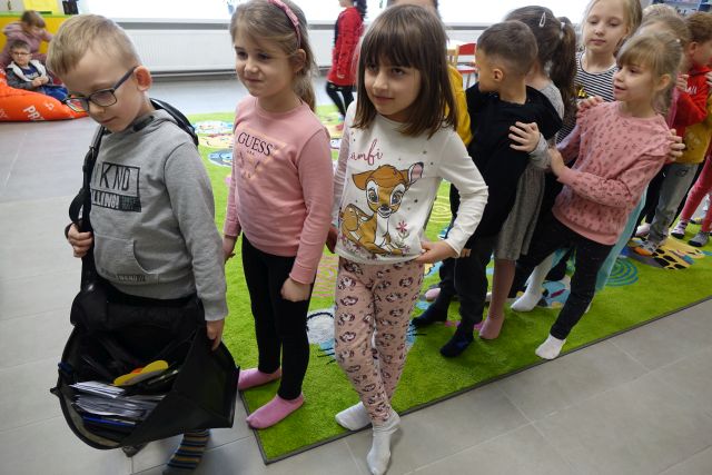 dzieci stoją w kolejce aby przymierzyć torbę listonosza, w tle regały z książkami