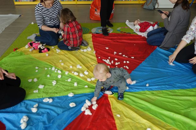 dzieci na kolorowej chuście bawią się kłębkami z waty