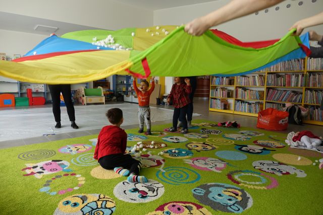 rodzice trzymają w górze kolorową chustę, na chuście śnieg z waty, a pod chusta dzieci