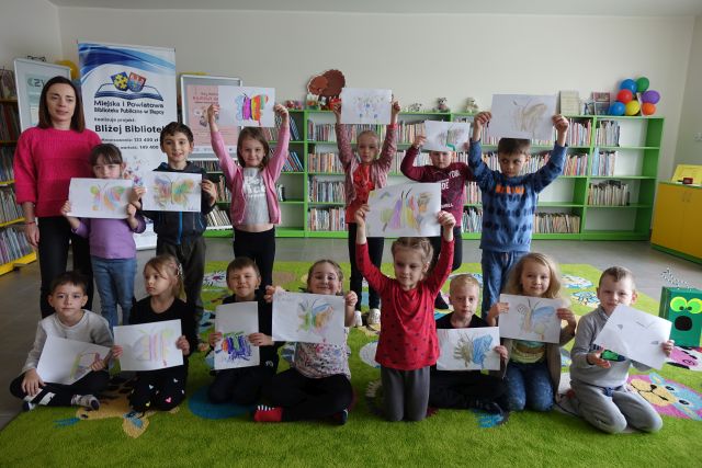 uczestnicy zajęć trzymają w dłoniach uniesione do góry wykonane przez siebie ilustarcje motyli