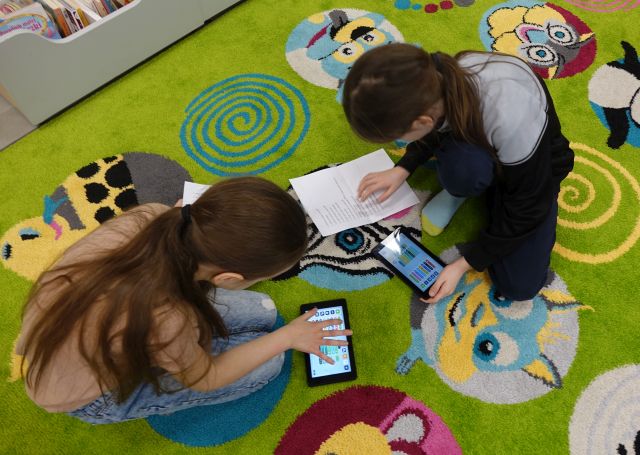 dwie dziewczynki za pomocą tabletów i zadania spisanego na kartce programują robota