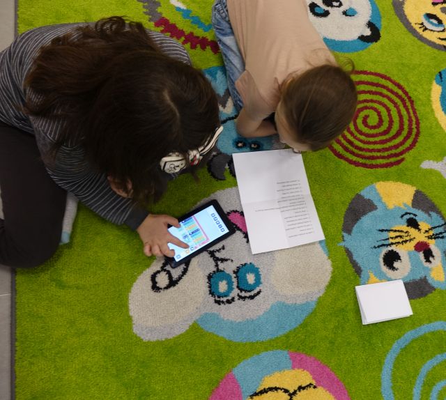 dwie dziewczynki za pomocą tabletów i zadania spisanego na kartce programują robota