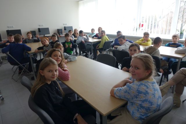 prawie 30 dzieci siedzi w sali komputerowej przy stołach