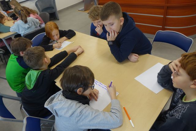 dzieci siedzą przy stole i notują na kartkach