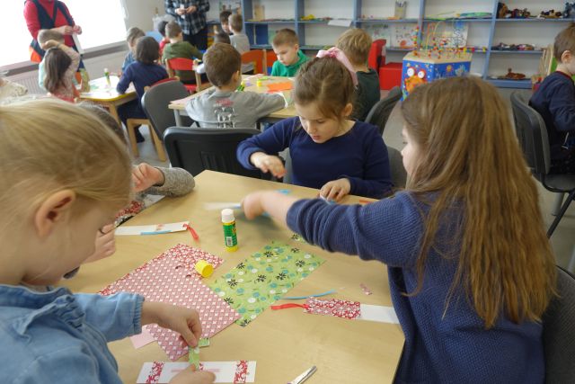 dzieci siedzą przy stołach i robią z kolorowych kartek zakładki do książki