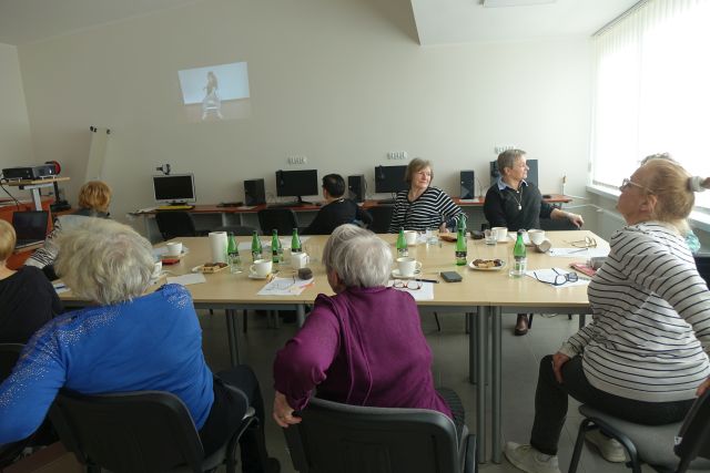 seniorki ćwiczą siedząc na krzesłach przy stołach