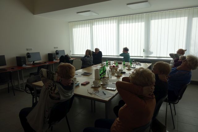 seniorki siedzą przy stołach i ćwiczą