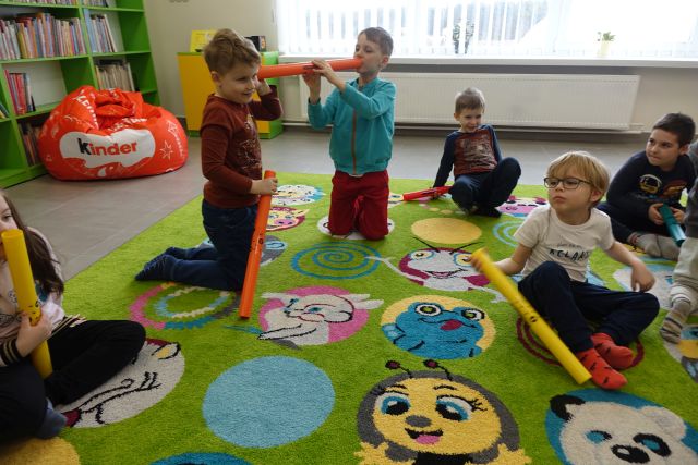 dzieci siedzą na kolorowym dywanie i bawią się bum bum rurkami w głuchy telefon