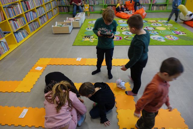 dzieci sterują za pomocą tabletów robotami, które jeżdżą po pomaranczowych puzlach