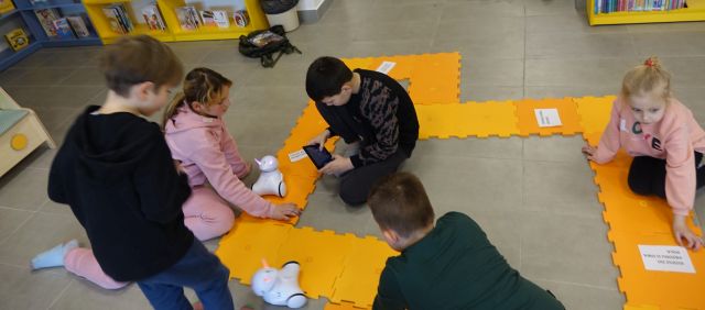 dzieci sterują za pomocą tabletów robotami, któe jeżdżą po pomarzńczowych puzlach