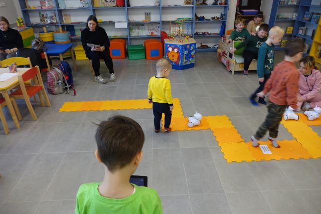 dzieci sterują za pomocą tabletów robotami, które jeżdżą po pomarańczowych puzlach