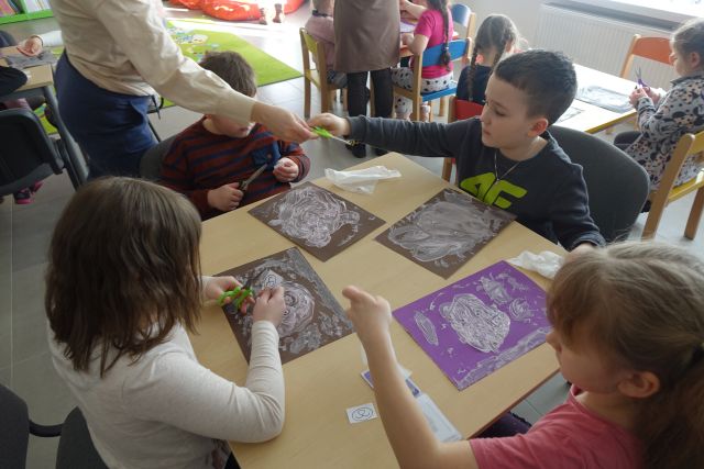 dzieci siedzą przy stolikach i malują pastą do zębów na kartkach niedźwiedzie