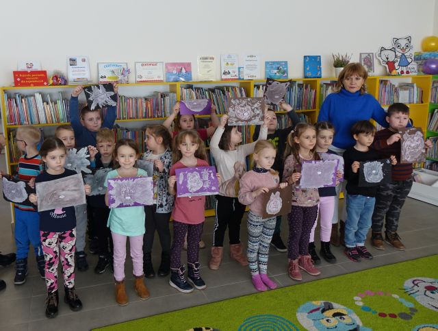 dzieci i przedszkolaki pozują do zdjęcia z wykonanymi przez siebie rysunkami z pasty do zębów, w tle regały z książkami