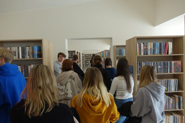 młodzież spaceruje pomiędzy regałami bibliiotecznymi