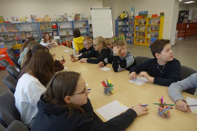 młodzież siedzi przy rzędzie połączonych stołów