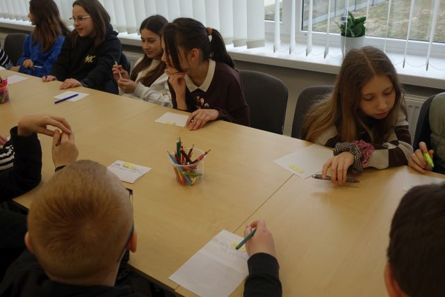 młodzież siedząca przy stałąch pisze na kartkach