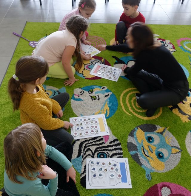 dzieci i kobieta siedzą na zielonym dywanie przed nimi leżą kartki z owadami