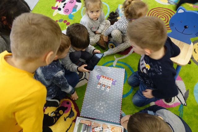 dzieci siedzą na zielonym dywanie i grają w grę planszową