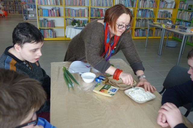 Kobieta kroi biały ser, w tle regały z książkami