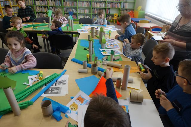 dzieci siedzące przy stołąch wykonują z rolek po papierze toaletowym, kolorowych kartek, wycinanek zwierzęta