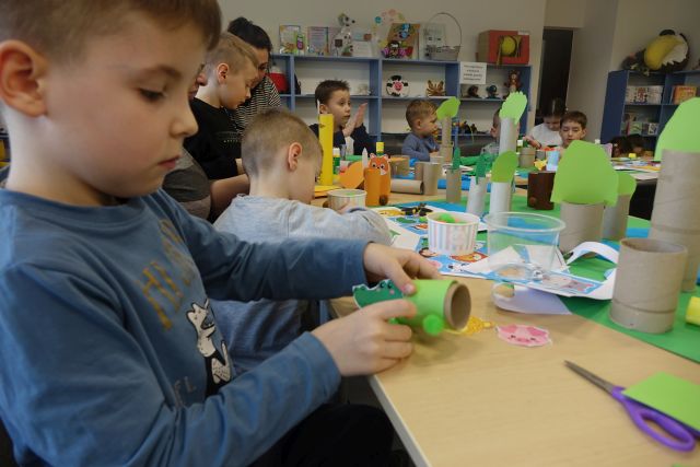 dzieci siedzące przy stołach wykonują z rolek po papierze toaletowym, kolorowych kartek, wycinanek zwierzęta